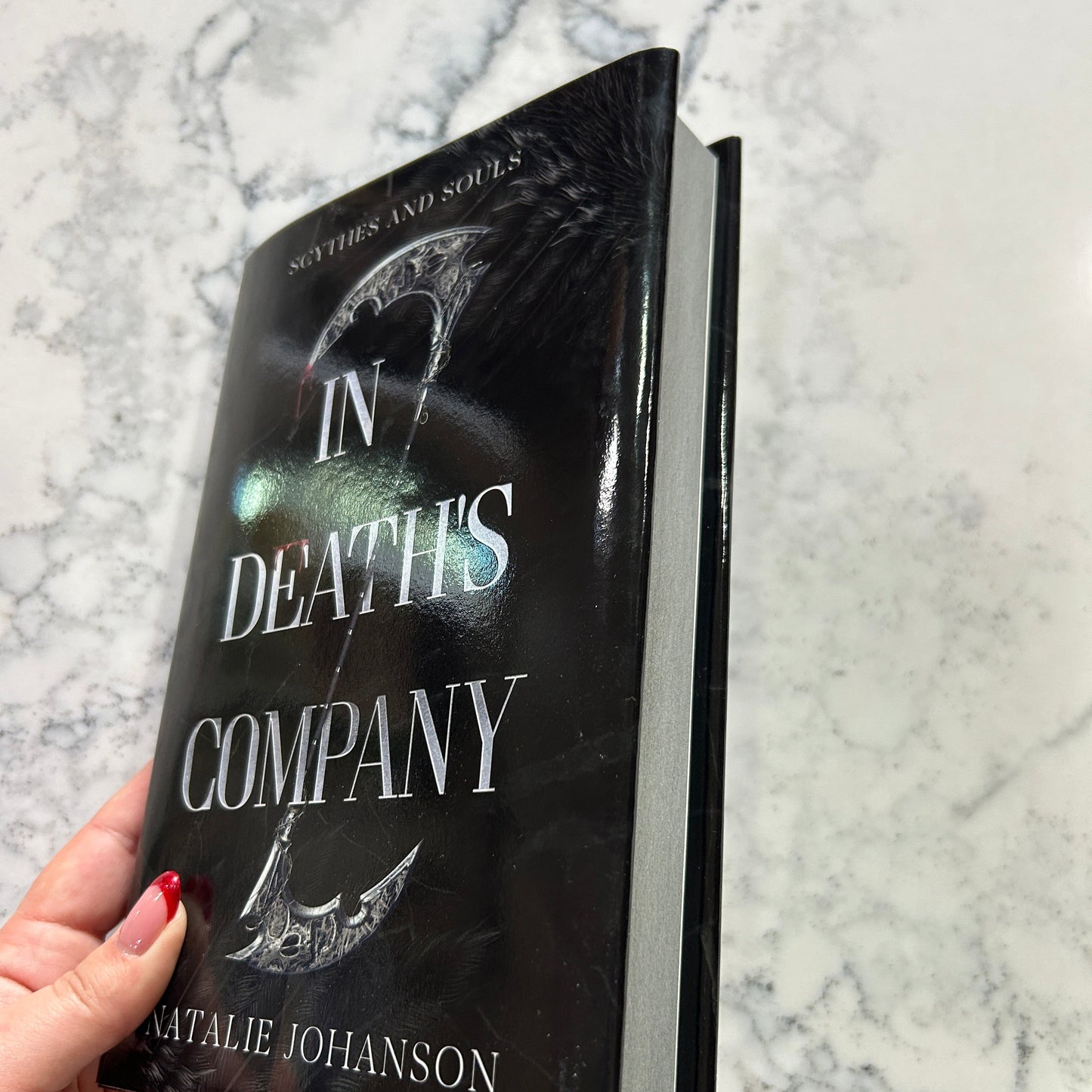 Book titled 'In Death's Company' held by a hand on a marble surface