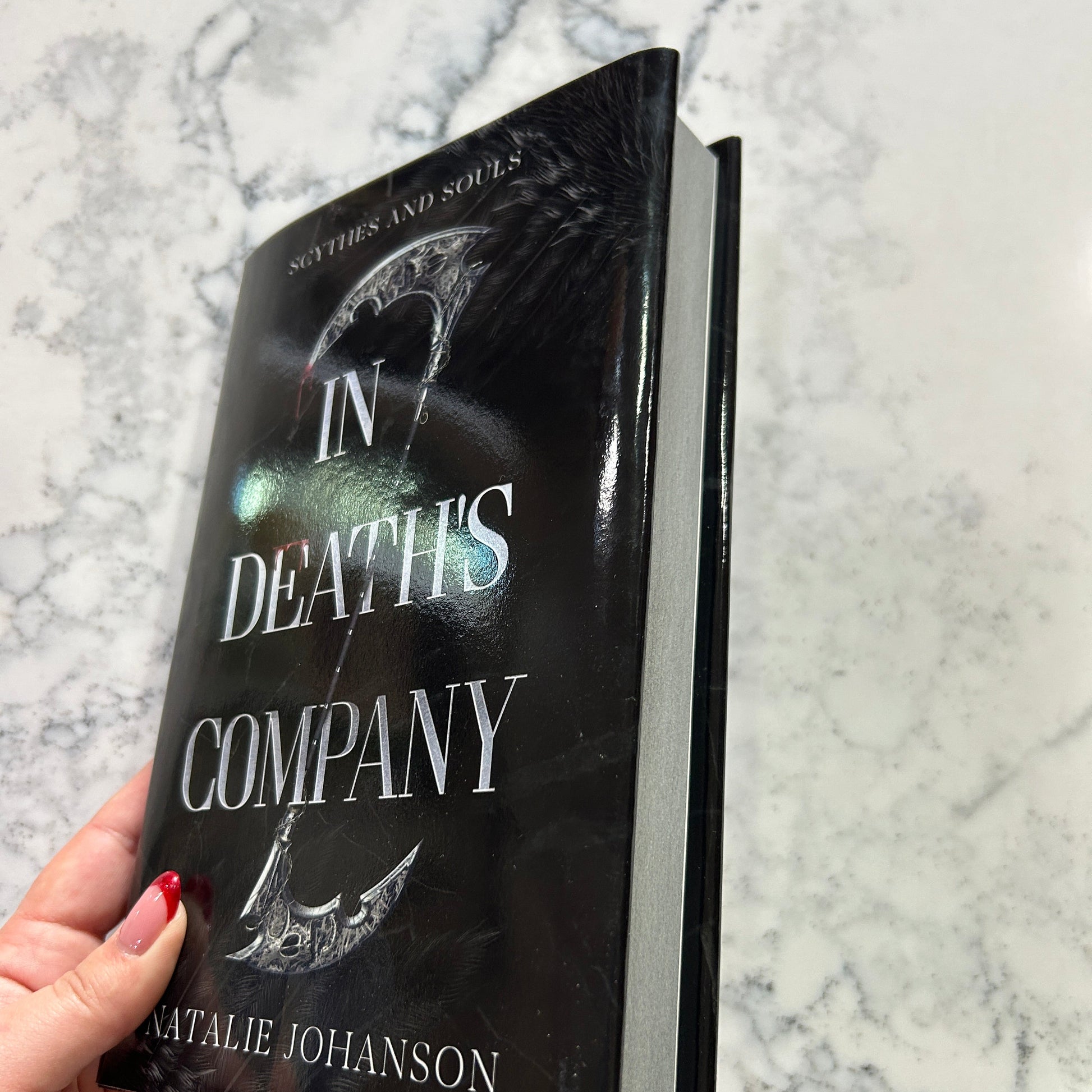 Book titled 'In Death's Company' held by a hand on a marble surface